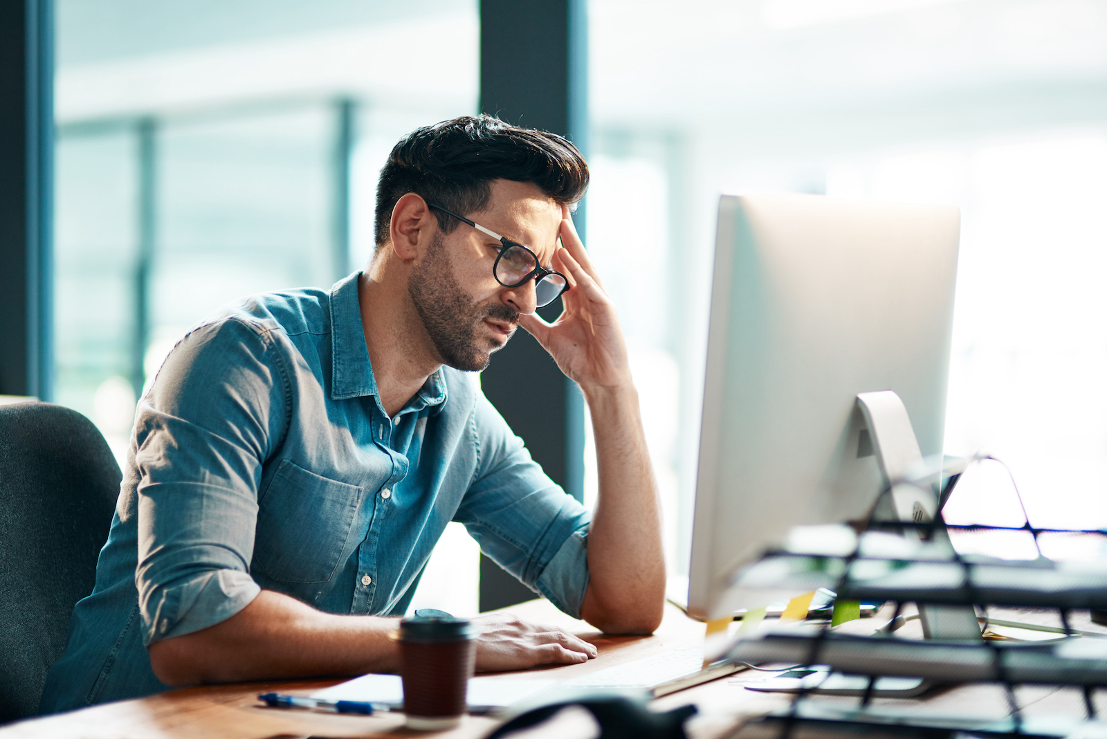 A man on the computer looking confused with his hand on his head.